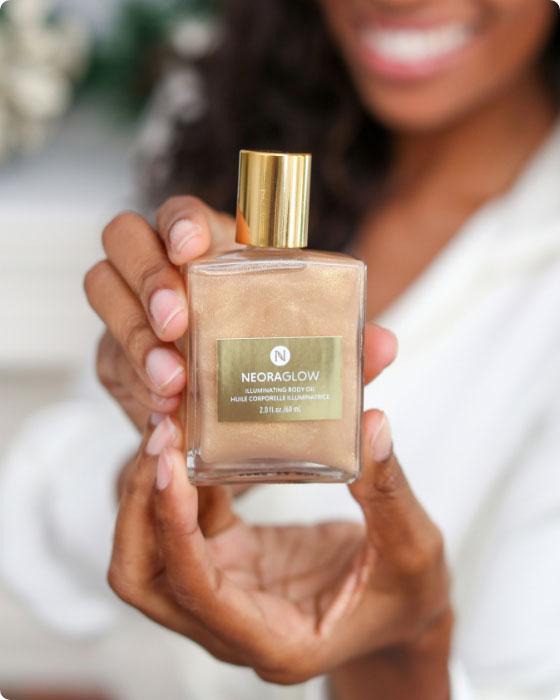 Woman smiling and holding Neora's hottest holiday limited-time must-have, Glisten Up Holiday Body Glow Oil. 